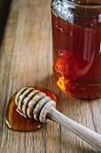 A jar of honey and a honey spoon on a wooden table