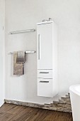 Storage space behind a bathroom door with a narrow wall cupboard and a towel rails and a natural stone skirting board