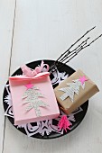 Hand-made, pink paper bag and gift decorated with paper Christmas trees on plate with doily and twigs
