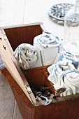 Rolled tea towels and vintage perforating tools in old wooden box with open lid