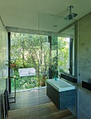 Designer bathroom with walk-in shower and view of white outdoor sofa in garden through glass wall