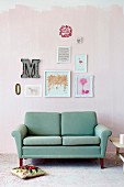 Hand-crafted artworks in various frames and ornamental letters on pink-painted wall above turquoise retro sofa