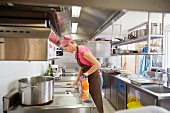 A woman wearing a headscarf cleaning in a restaurant kitchen