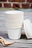 A stack of take-away cups and wooden forks on a table outside