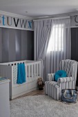 Striped, grey armchair next to cot in nursery with blue accents