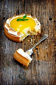 A lemon meringue tartlet on a wooden surface with a bite taken out of it