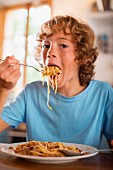 A teenage boy eating spaghetti at a dining table