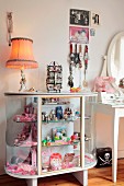 Display case decorated with pink toys, jewellery and table lamp in vintage-style girl's bedroom