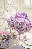 Bouquet of purple hydrangeas in glass vase next to basket of dried lavender