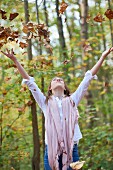 A teenager in an autumn forest throwing leaves in the air