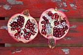 A halved pomegranate on a red wooden surface (seen from above)
