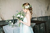 Fairy-tale bride holding bouquet and wearing flower wreath in vintage interior