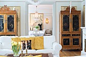 White sofa, antique cupboards with carved and painted panels in living room with view in to dining room through open doorway