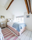 Pink and white striped runner on white wooden floor and single bed next to window in rustic bedroom