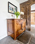 Vase of tulips on simple, wooden cabinet on old stone floor in front of open doorway in rustic board wall