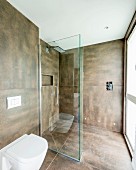 Toilet next to glazed, floor-level shower area in modern bathroom with large brown tiles on walls and floor