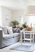 White-painted side table, comfortable couch and pendant lamp with wwhite fabric lampshade in corner of simple living room