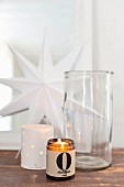 Tealights in holders and glass jar in front of white paper star