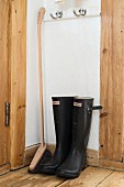 Black Wellington boots and long-handled brush in corner