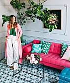 Young woman in interior with hot pink sofa, glass table, tiled floor and lemon tree