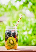 Fruity iced tea in a screw-top jar with a straw on a garden table