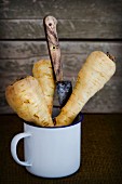 Fresh parsnips in a metal cup against a rustic background