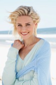 Blonde Frau in hell mintfarbenem Wollpulli und hellblauem Pulli um die Schultern am Strand