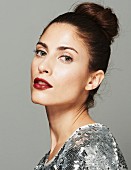 A brunette woman wearing a sequinned top and dark red lipstick with her hair up
