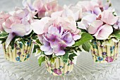 Silk flowers and ivy in colourful paper cake cases decorating table