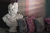 Büste des Gottes Apollo auf antikem Tisch mit grauen und pinkfarbenen Samtkissen