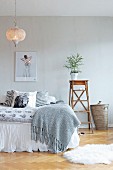 Small conifer on stepladder next to bed with scatter cushions and blanket below Oriental pendant lamp