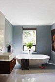 Freistehende Badewanne in elegantem Bad, mittelgrau getönte Wände und teilweise Boden, im Vordergrund polierter, weisser Fliesenboden