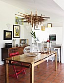 Kugelvase auf Holztisch unter von Decke abgehängtem Kunstobjekt aus Holzstäben, im Hintergrund offene Küche mit Theke