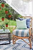 Rattanstuhl mit Kissen und gestreiftem Sitzpolster neben Armierungsgitter mit aufgehängten Lavendeltöpfen in Gartenpavillon