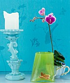 Pale blue candlestick, green glass vase and orchid in vintage-style coffee cup
