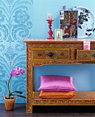 Accessories on console table richly decorated with floral pattern against blue wall