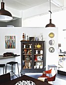 Ornaments in glass-fronted cabinet against free-standing partition, industrial-style pendant lamps above dining table