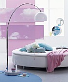 Rundes Bett, Stehleuchte mit Marmorfuss und rosa Fotodrucken mit Wolkenmotiven als Wanddekoration