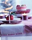 Tischgedeck weihnachtlich dekoriert mit rotem Apfel, Kerze und Dekoband