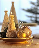 Festive arrangement of gold baubles and candles shaped like Christmas trees on gold plate