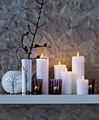 Atmospheric arrangement of vases, tealight holders and pillar candles on white, wall-mounted shelf