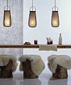 Baumstämme mit Schaffellen als Sitzgelegenheiten an rustikalem Holztisch mit dekorativen Bambus-Hängeleuchten