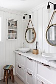 Washstand with twin, white countertop sinks and drawers in base cabinet below mirrors on white wooden wall
