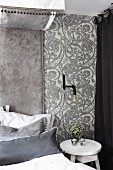 Bett und weisser Nachttisch vor tapezierter Wand mit Ornament Muster