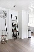 Ladder shelves used as drinks cabinet next to candle lantern on side table below station clock in open-plan interior