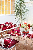 Mit roten Accessoires gedeckter Bistrotisch und weiße Vintage-Metallstühle in gefliestem Innenhof