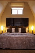 Bett mit Kissen vor dunkelbraunem Lederkopfteil, flankiert von künstlerischen Leuchten im Dachgeschosszimmer