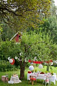 Blick von oben in Garten auf gedeckten Tisch unter Baum mit weissen Lampions, Flusskrebsfest in Schweden