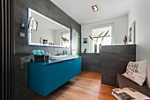 Zeitgenössisches Bad mit petrolfarbenem Waschtisch unter Spiegel, an Wand und Brüstungsmauer graue Fliesen