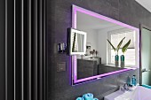 A wall mirror with integrated pink LED lighting on a grey-tiled wall